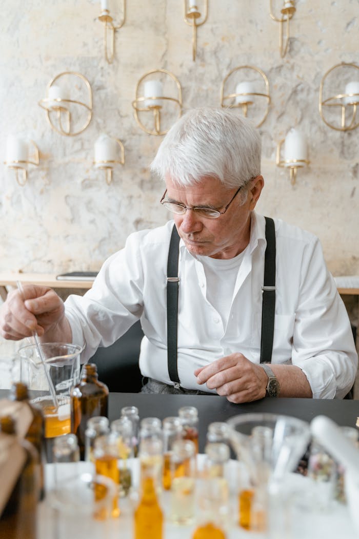 Elderly man mixing liquids in a laboratory setting for perfume making.